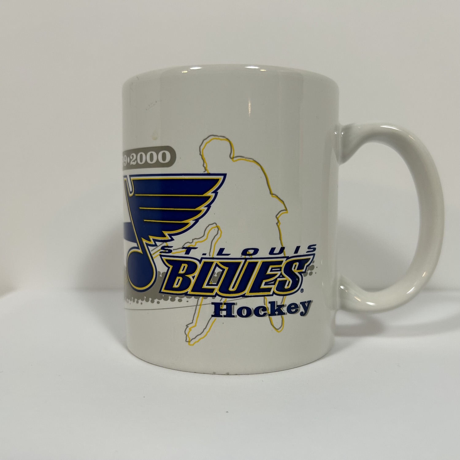 white coffee mug with blues logo on top of hockey player silouette