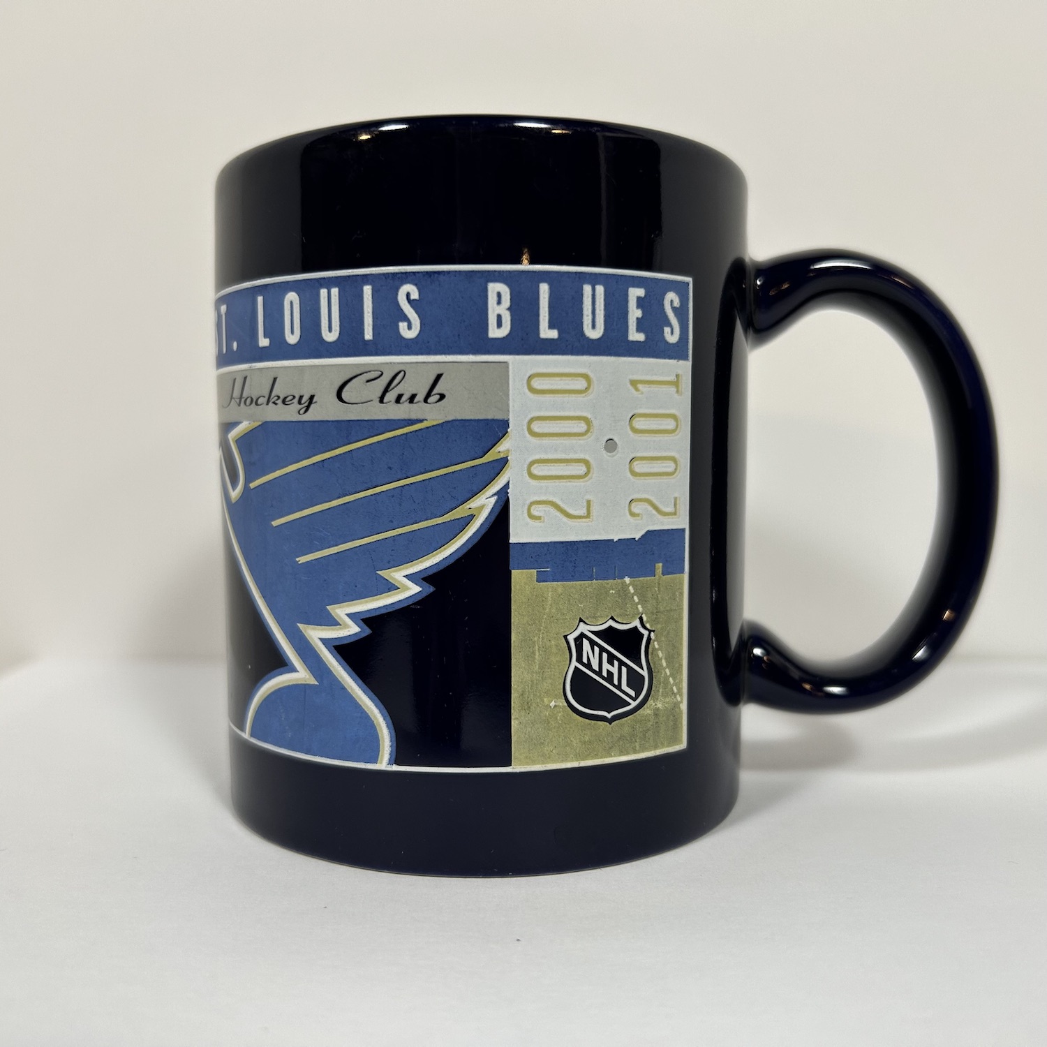 Navy coffee mug with grid graphic containing blues logo, nhl shield, and 2000-2001