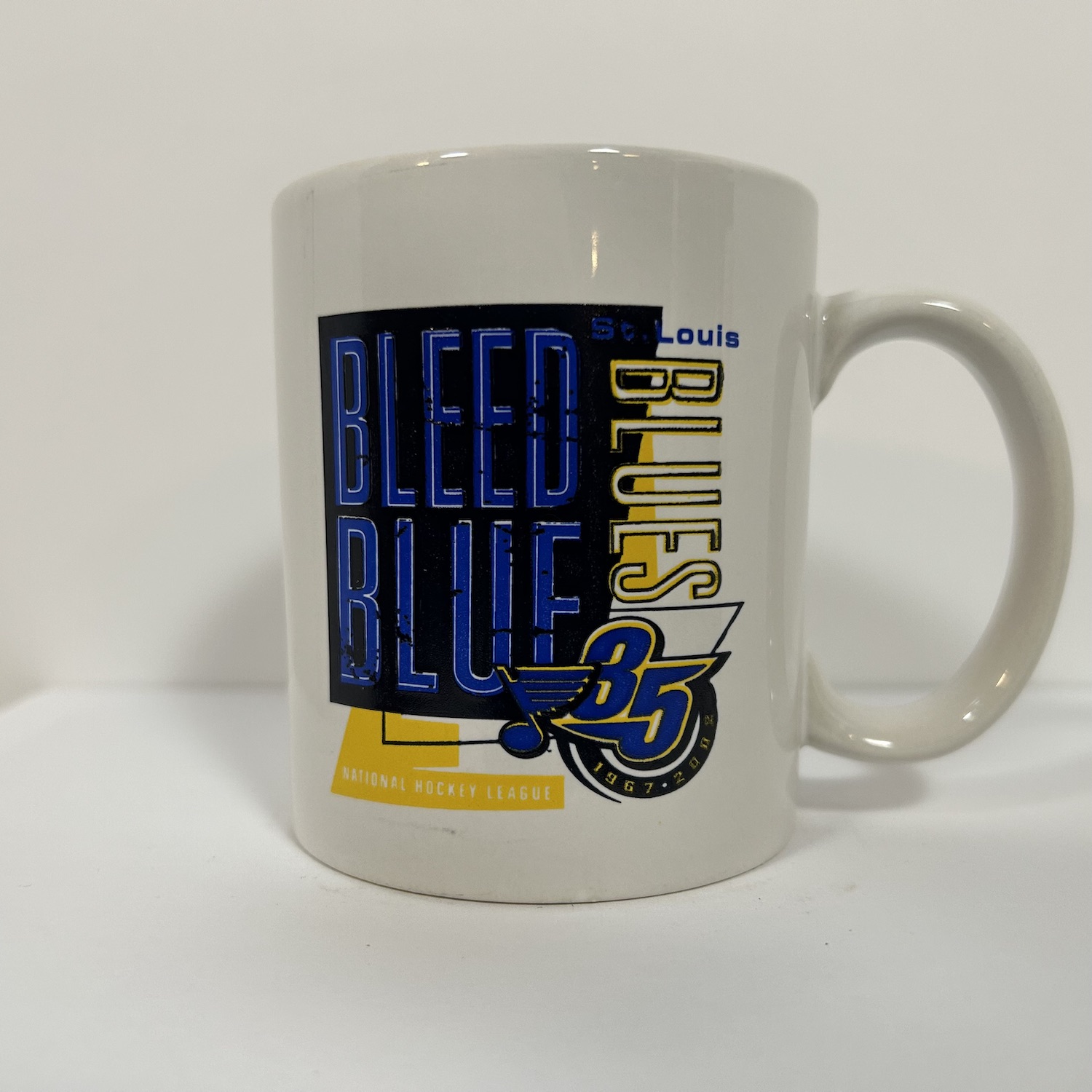 white coffee mug with a slogan that says Bleed Blue, and a 35th anniversary logo