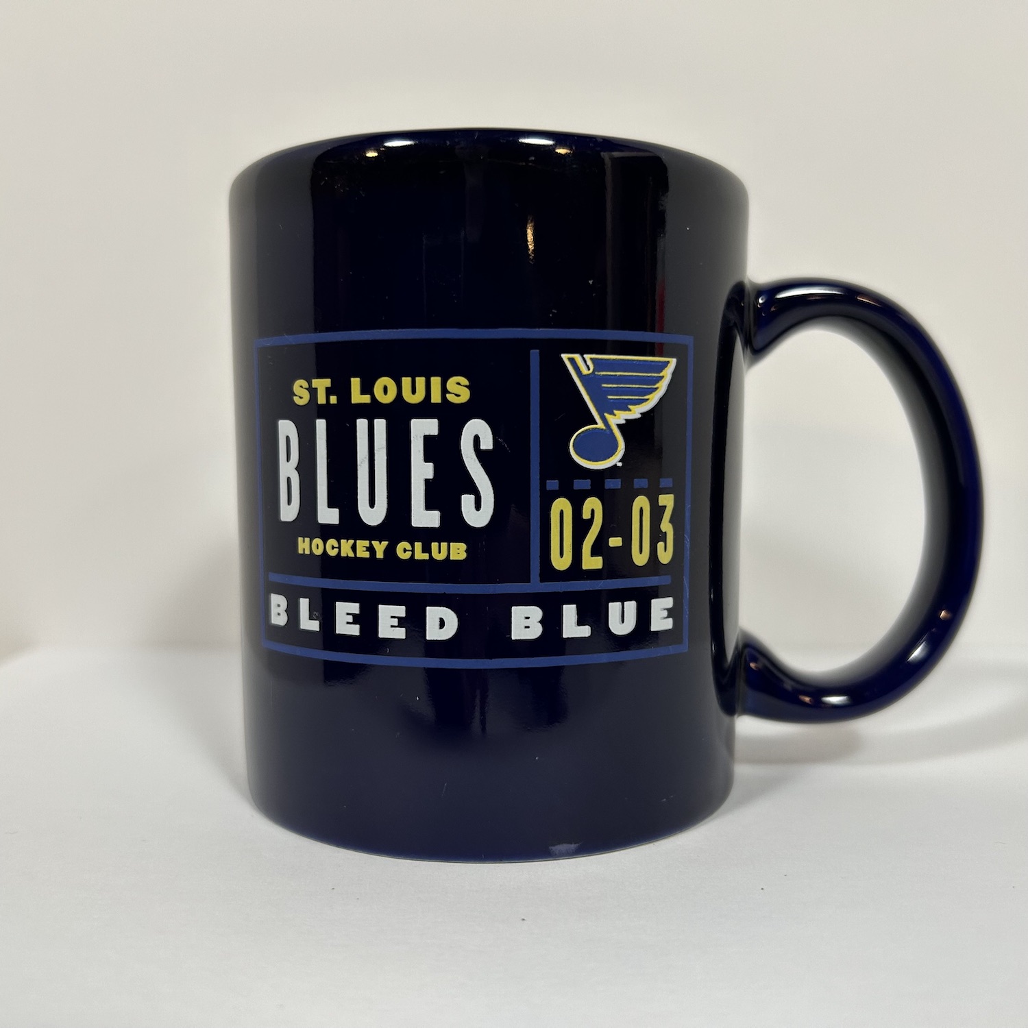 Navy coffee mug with grid that has the word St. Louis Blues Hockey Club, the blues logo, the years 02 to 03, and the bleed blue slogan