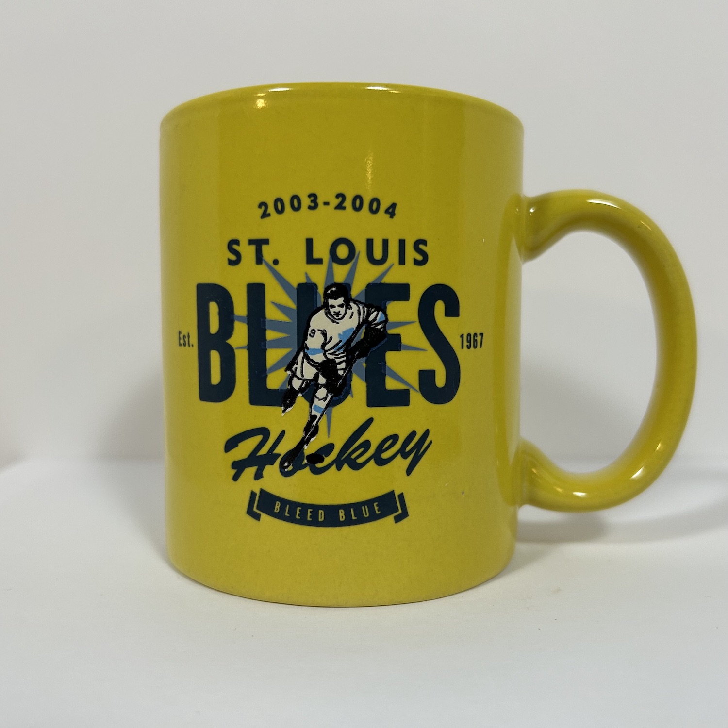 1950s themed yellow coffee mug with hockey player on top of St. Louis Blues words and bleed blue slogan underneath