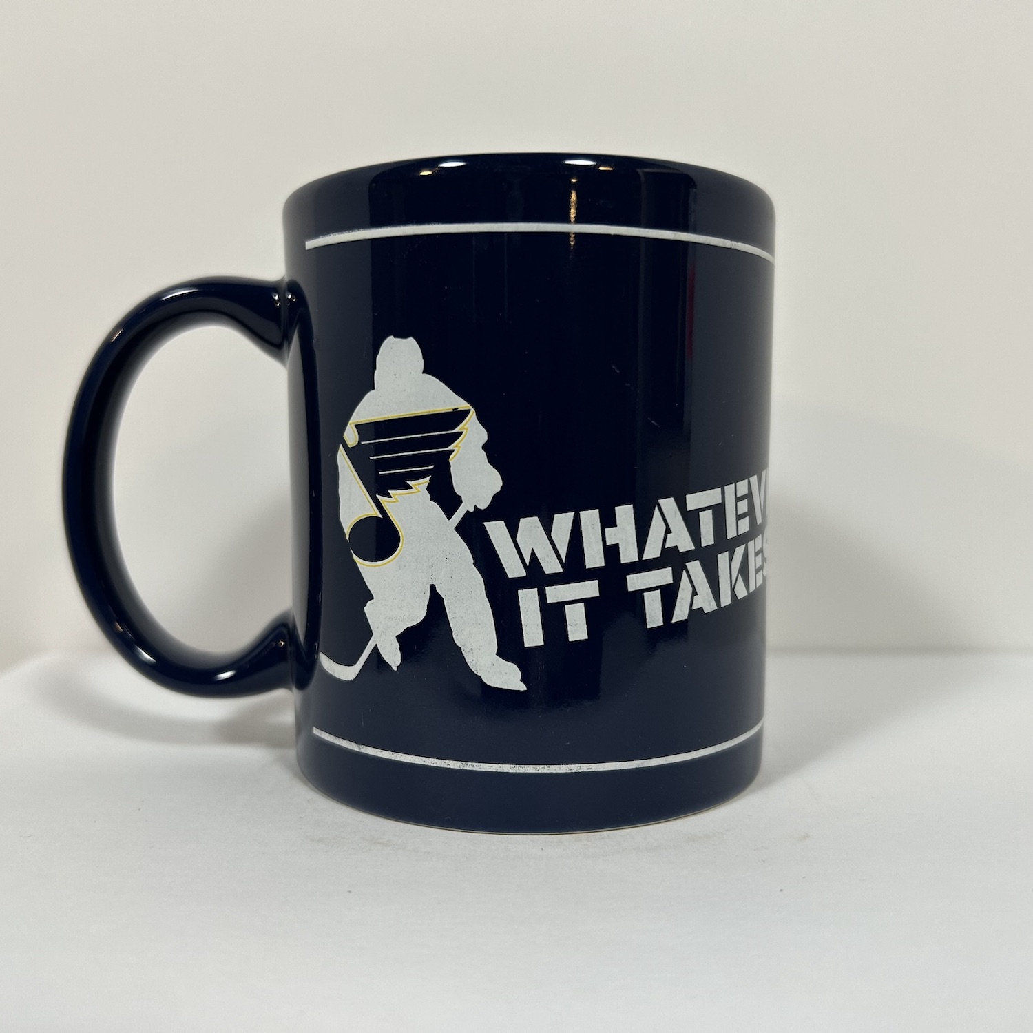 light navy coffee mug with a blues logo inside a hockey player silouette and the slogan Whatever It Takes